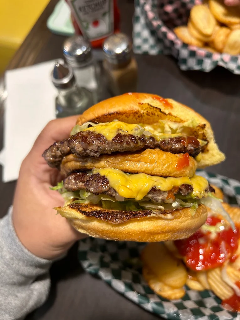 A hand holding a towering double cheeseburger, with melted cheese, pickles, and a toasted middle bun