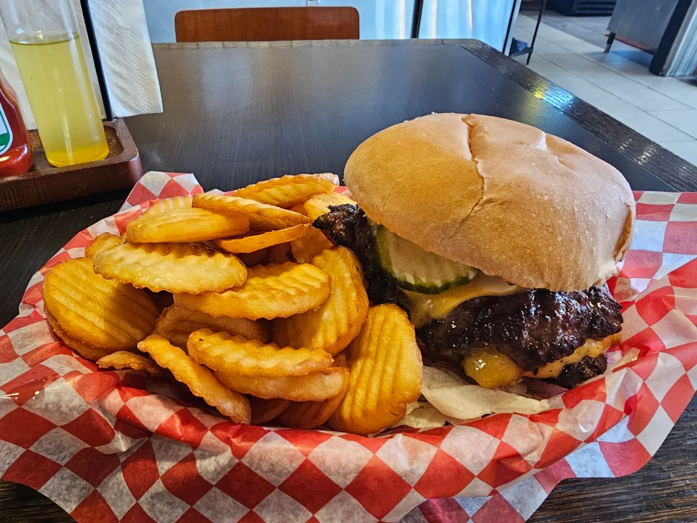A double smash cheeseburger with pickles and golden crinkle cut dollar fries, served on red checkerboard paper
